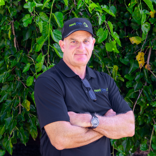 A person wearing a black polo shirt and cap stands with arms crossed. The cap and shirt have