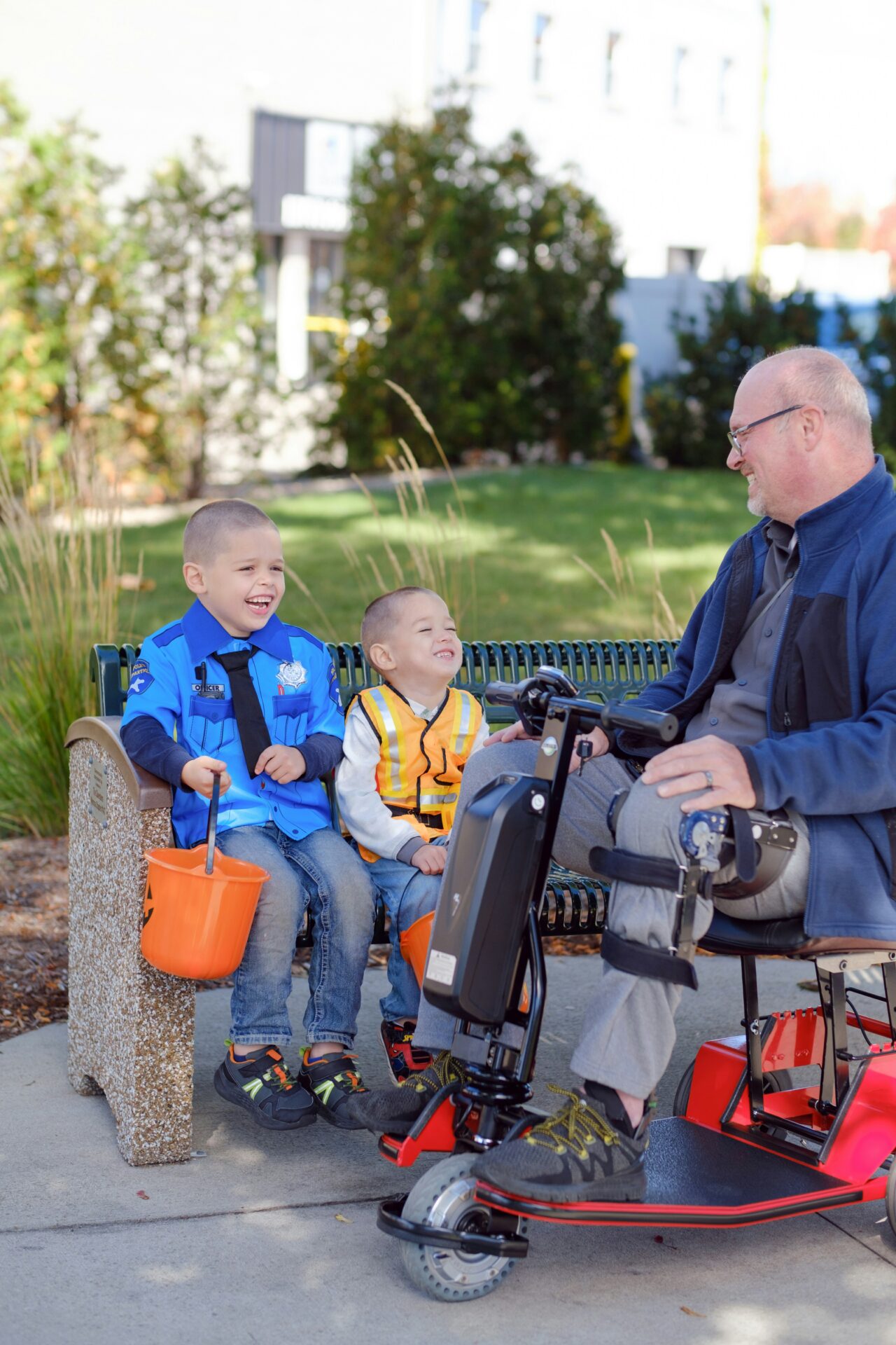 man on a mobility scooter smiling at 2 children holding halloween buckets